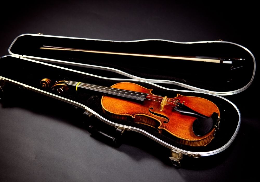 Violin and its bow in a case, on black background
