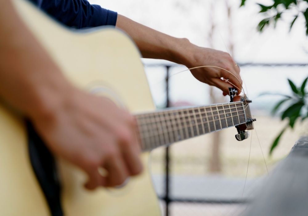 A guitarist adjusting his acoustic guitar