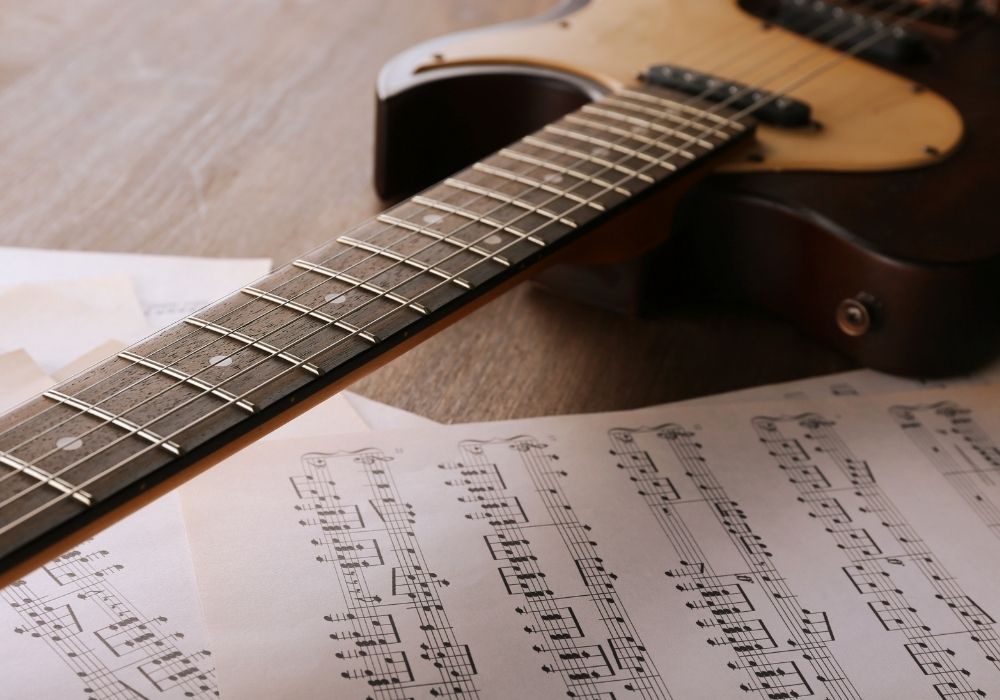 electric guitar with music notes for electric guitar song on wooden table close up