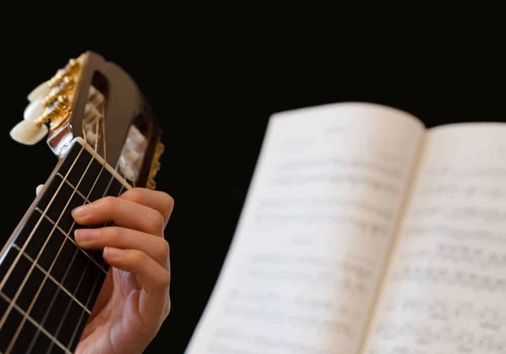 a guitarist strumming his guitar while following a great guitar book to play a song